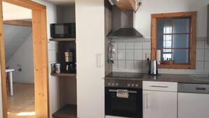 A compact kitchen with a microwave, stove, and oven, wooden beams, and a window with a view. - Vacation apartment B, Salzgasse, Old Town - Edition Bad Wimpfen (Bad Wimpfen)