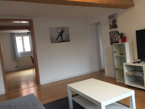 A living room with a white table, a TV on a stand, and a painting on the wall.