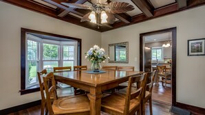 Une salle à manger avec une table et des chaises en bois, un ventilateur de plafond et de grandes fenêtres.