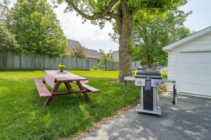 A backyard with a picnic table, a barbecue grill, and a garage. - Charming Clayton Village Retreat – Walk to River, Shops & Sunset Views! (Clayton)