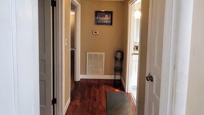 A hallway with wooden flooring, white doors, a ceiling light fixture, a thermostat, and a framed picture on the wall. - All in Reach, 2BR in West End (Nashville)