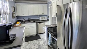 A modern kitchen with white cabinets, stainless steel appliances, a microwave, and a refrigerator. - All in Reach, 2BR in West End (Nashville)