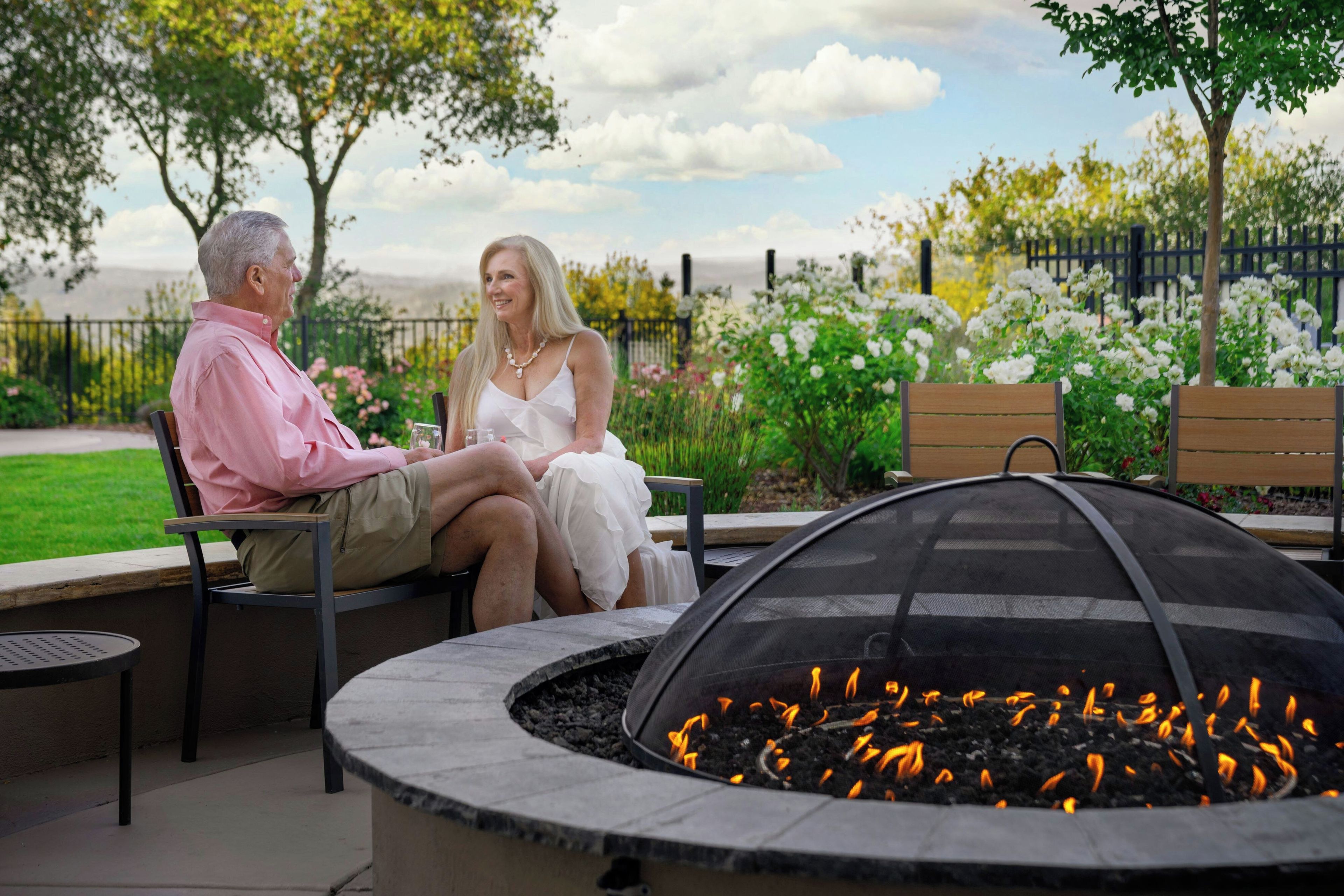 A couple seated at an outdoor table with a fire pit in the foreground.