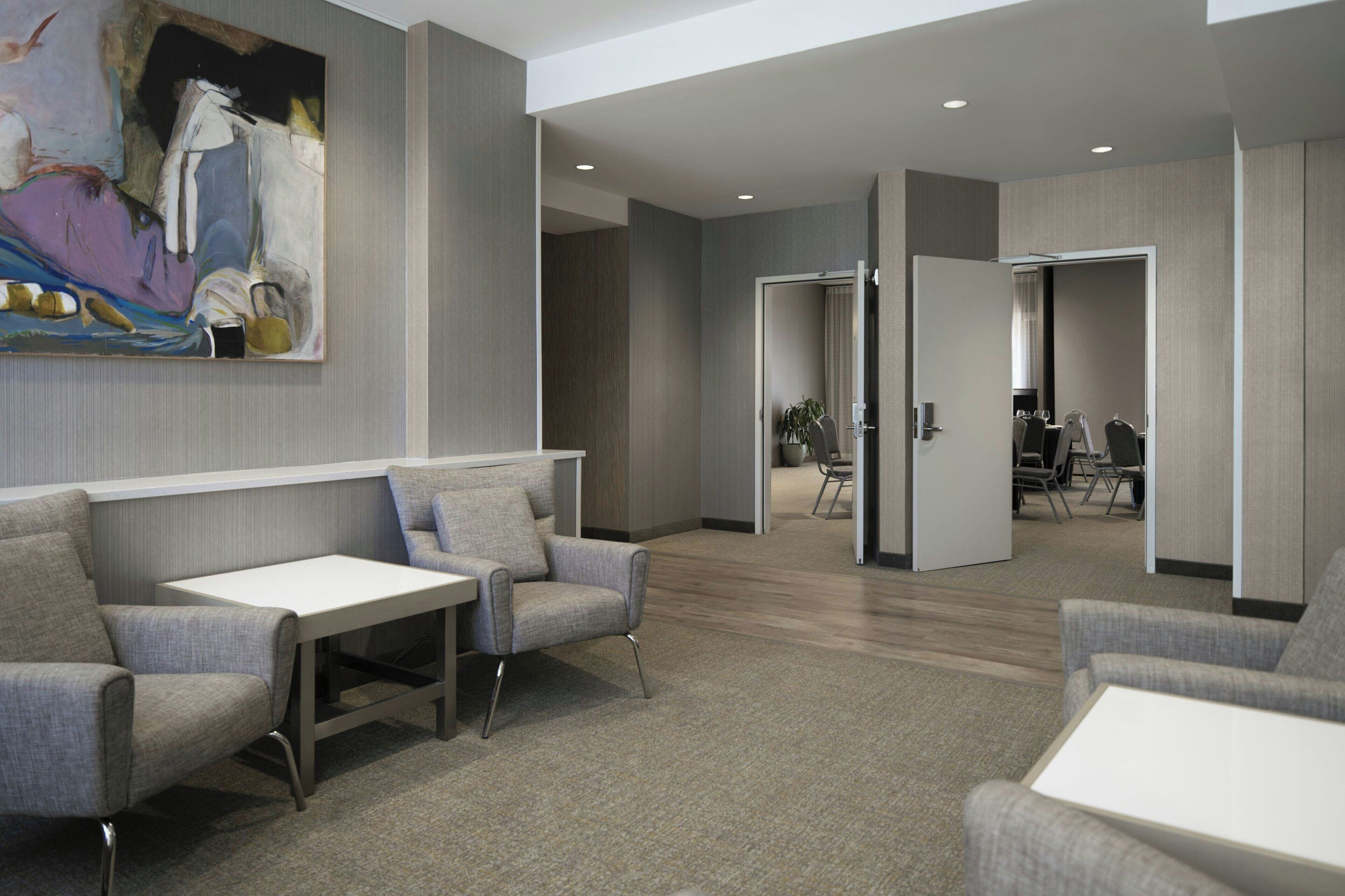 Un moderno vestíbulo de hotel con asientos tapizados en gris, una mesa blanca y un cuadro abstracto grande en la pared.