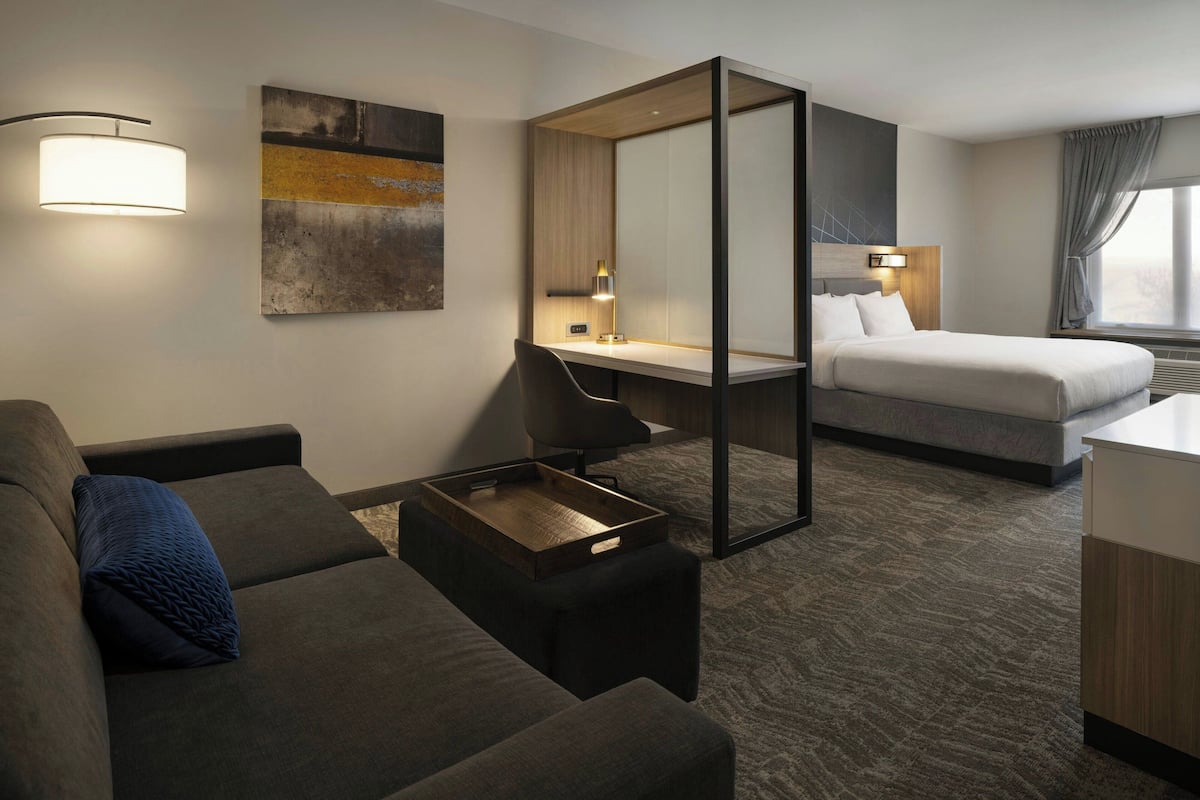 A hotel room with a sofa, a desk, a bed, and a large window.