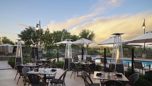 An outdoor patio area with tables and chairs, a pool, and string lights. - Hotel Vista Sierra (Auburn)