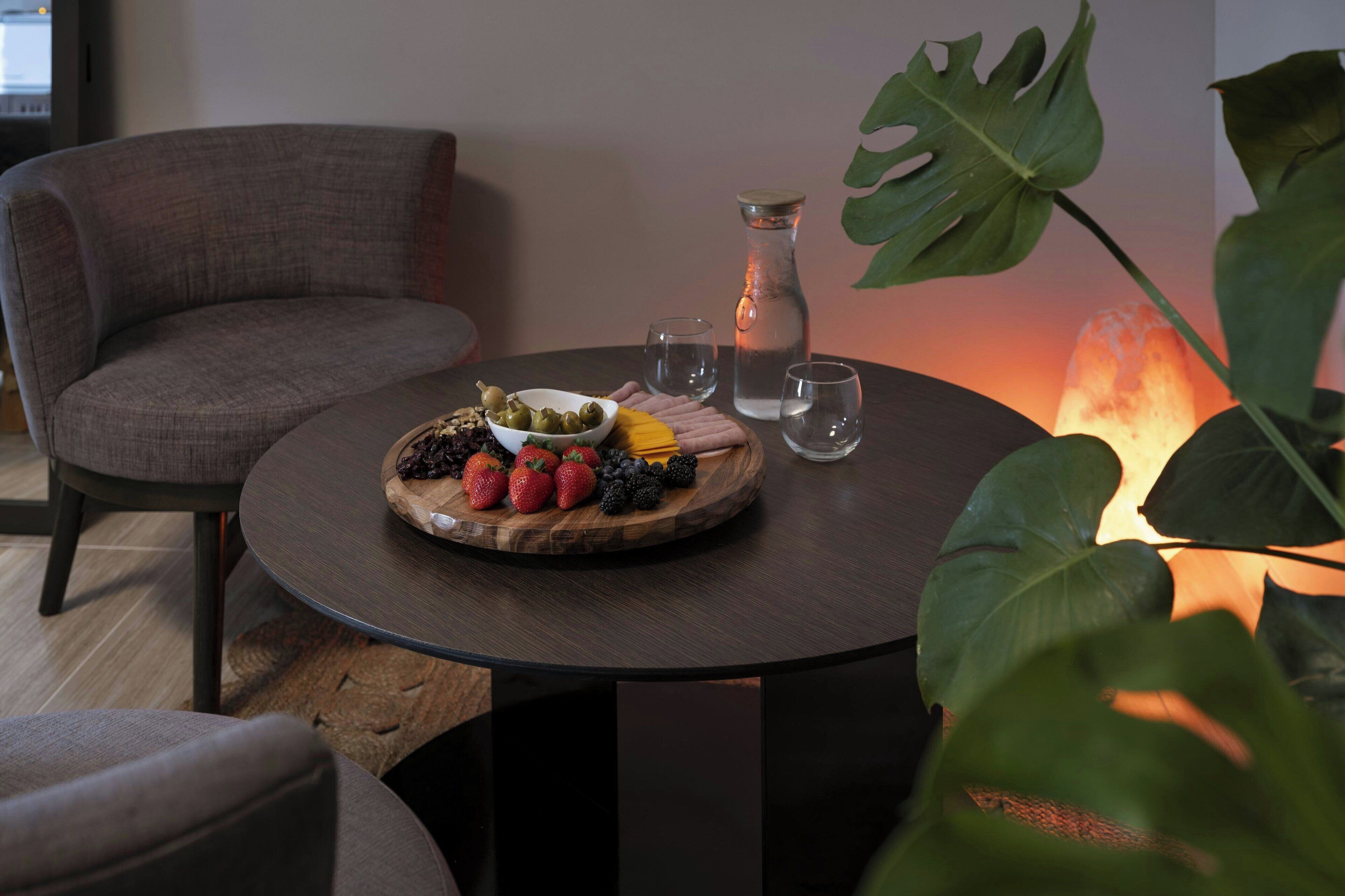 A round table with a fruit platter, a glass pitcher, and two glasses.