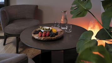 A round table with a fruit platter, a glass pitcher, and two glasses.