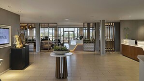 A spacious lobby with a reception desk, a large potted plant, and a seating area with chairs and tables. - Hotel Vista Sierra (Auburn)