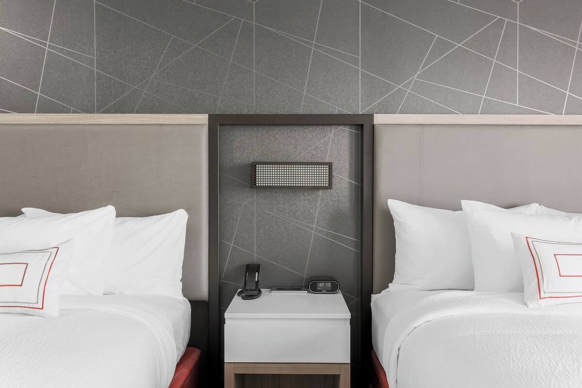 A hotel room with two beds, a nightstand, a small table, and a wall-mounted charging station.
