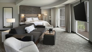 A modern hotel room with a large bed, a sofa, a chair, a TV, and a balcony with a view. - Hotel Vista Sierra (Auburn)