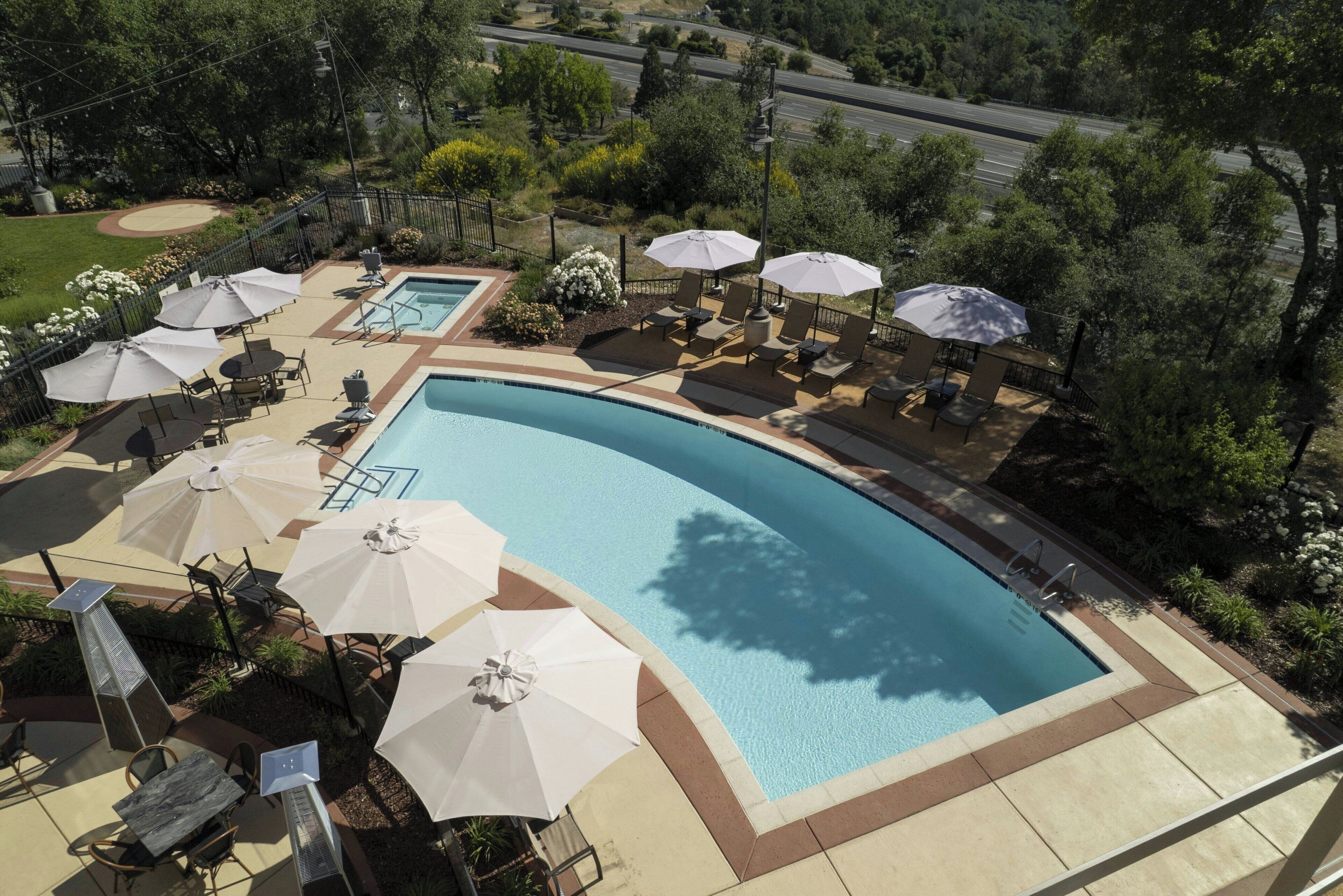 A swimming pool with lounge chairs and umbrellas, surrounded by greenery and a paved deck.