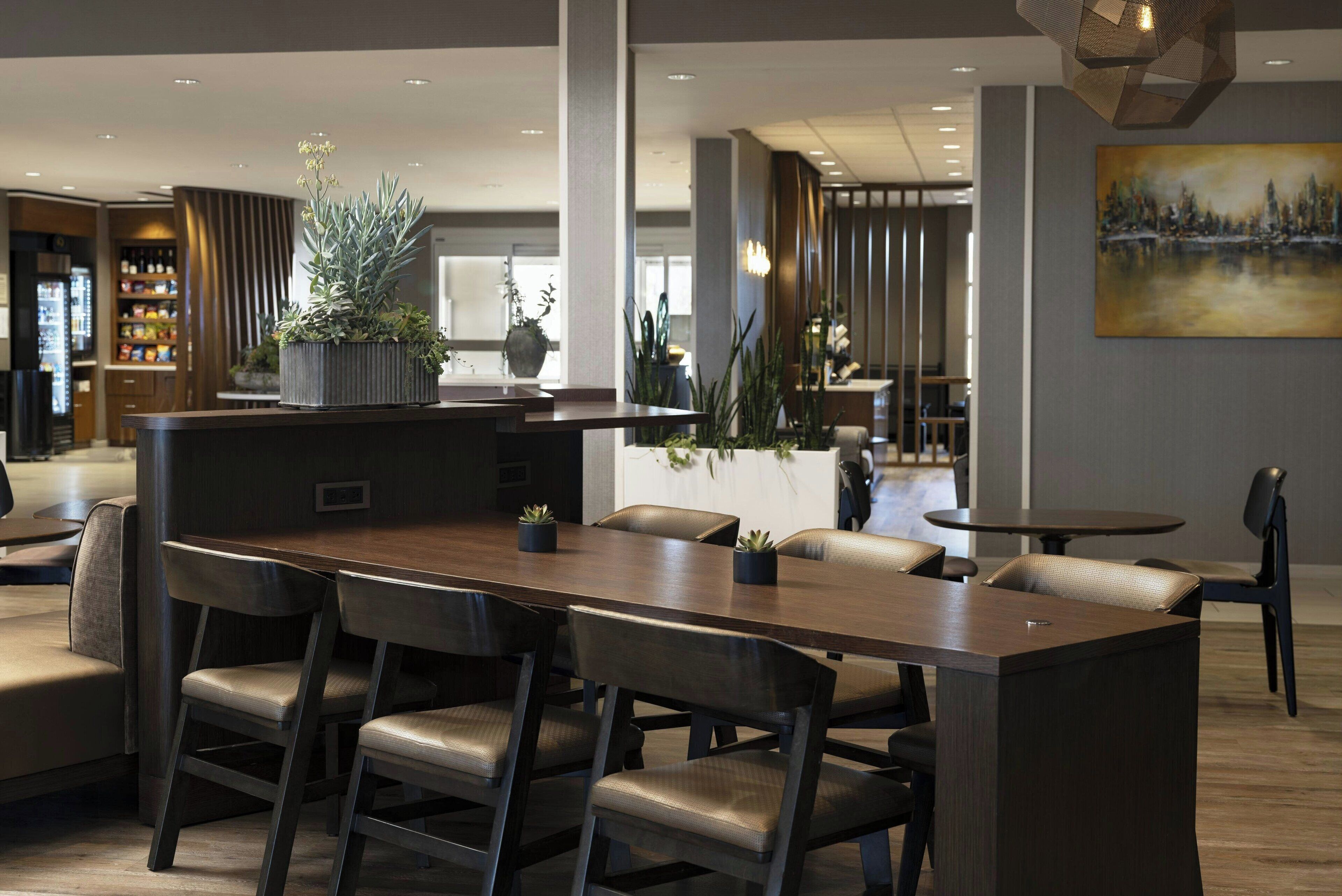 A modern dining area with a long table, several chairs, and potted plants.