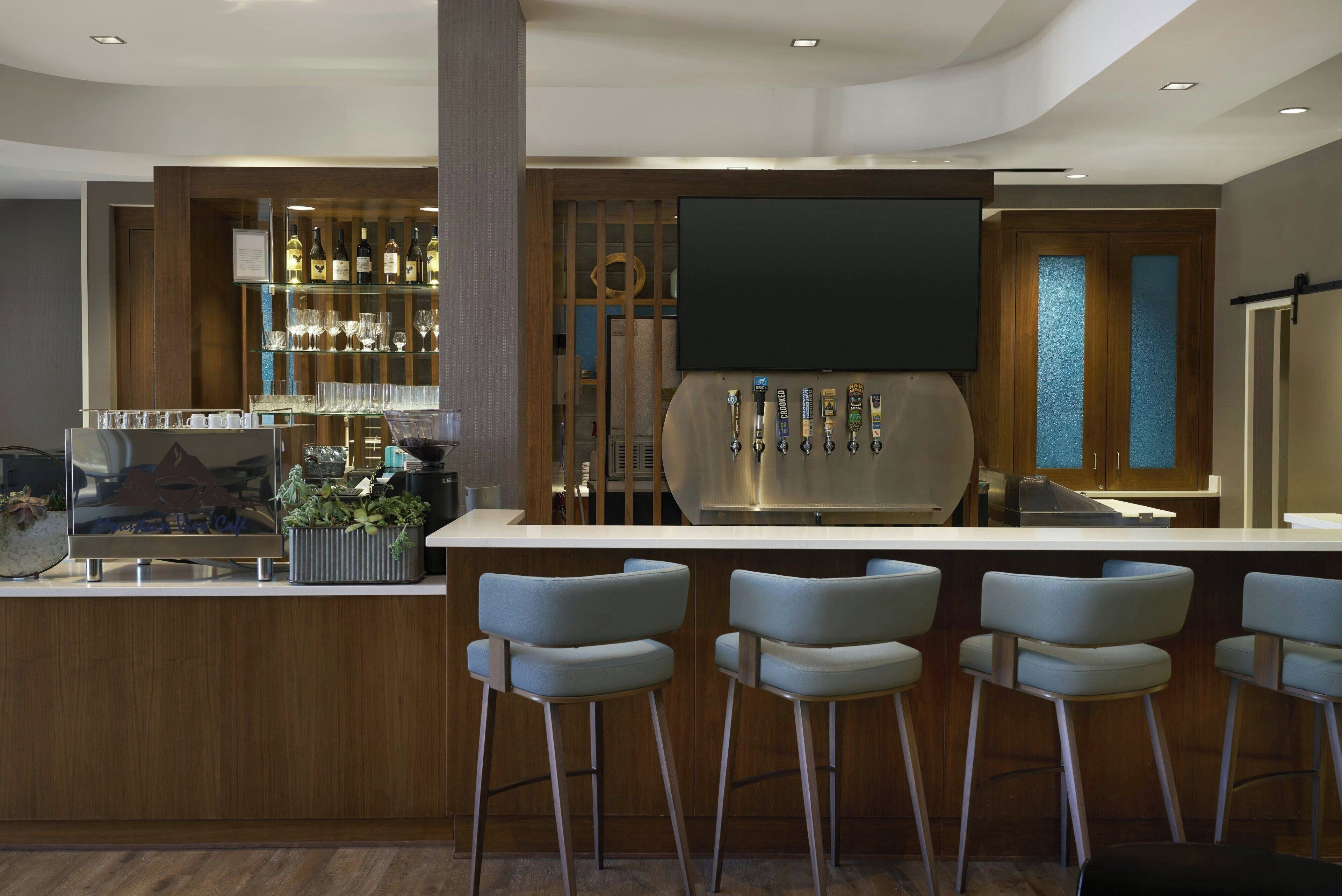 A modern bar area with a long counter, multiple stools, and a variety of bottles and glasses.
