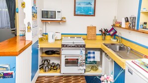 Eine kleine Küche mit Mikrowelle, Backofen und Spüle. Es sind verschiedene Küchenutensilien und ein Kalender an der Wand vorhanden.