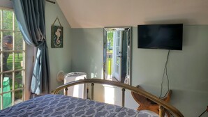 Un dormitori amb un llit, una televisió penjada a la paret, una finestra amb cortines i una porta que dóna a l'exterior.