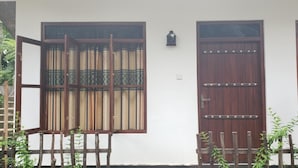 A traditional house with two wooden doors and windows, a small wall-mounted lantern, and a wooden fence with plants. - Tanoaks Villa (Mirissa)