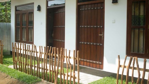 A building with three wooden doors, a small window, and a wooden fence. - Tanoaks Villa (Mirissa)