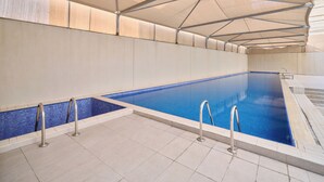 An indoor swimming pool with a tiled floor, metal pool ladders, and a canopy overhead. - Code Housing - Fintas (Fintas)