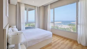A hotel room with a large bed, a bedside lamp, a view of the sea, and a window with curtains. - Code Housing - Fintas (Fintas)