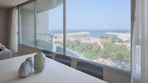 A modern room with a large window overlooking a coastal view, a white table with vases, and a grey sofa. - Code Housing - Fintas (Fintas)