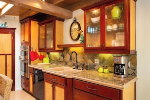 Una cocina con armarios de madera, un lavabo, una cafetera y un reloj en la pared.