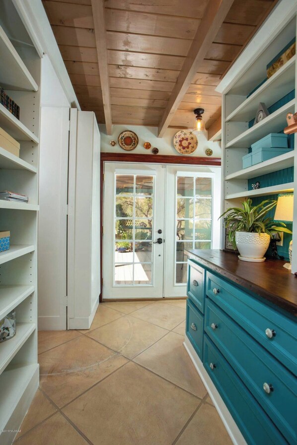 Una cocina con armarios blancos, encimera color turquesa y techo de madera.