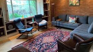 Un salon chaleureux avec un canapé bleu, un tapis à motifs et une grande fenêtre avec des volets.