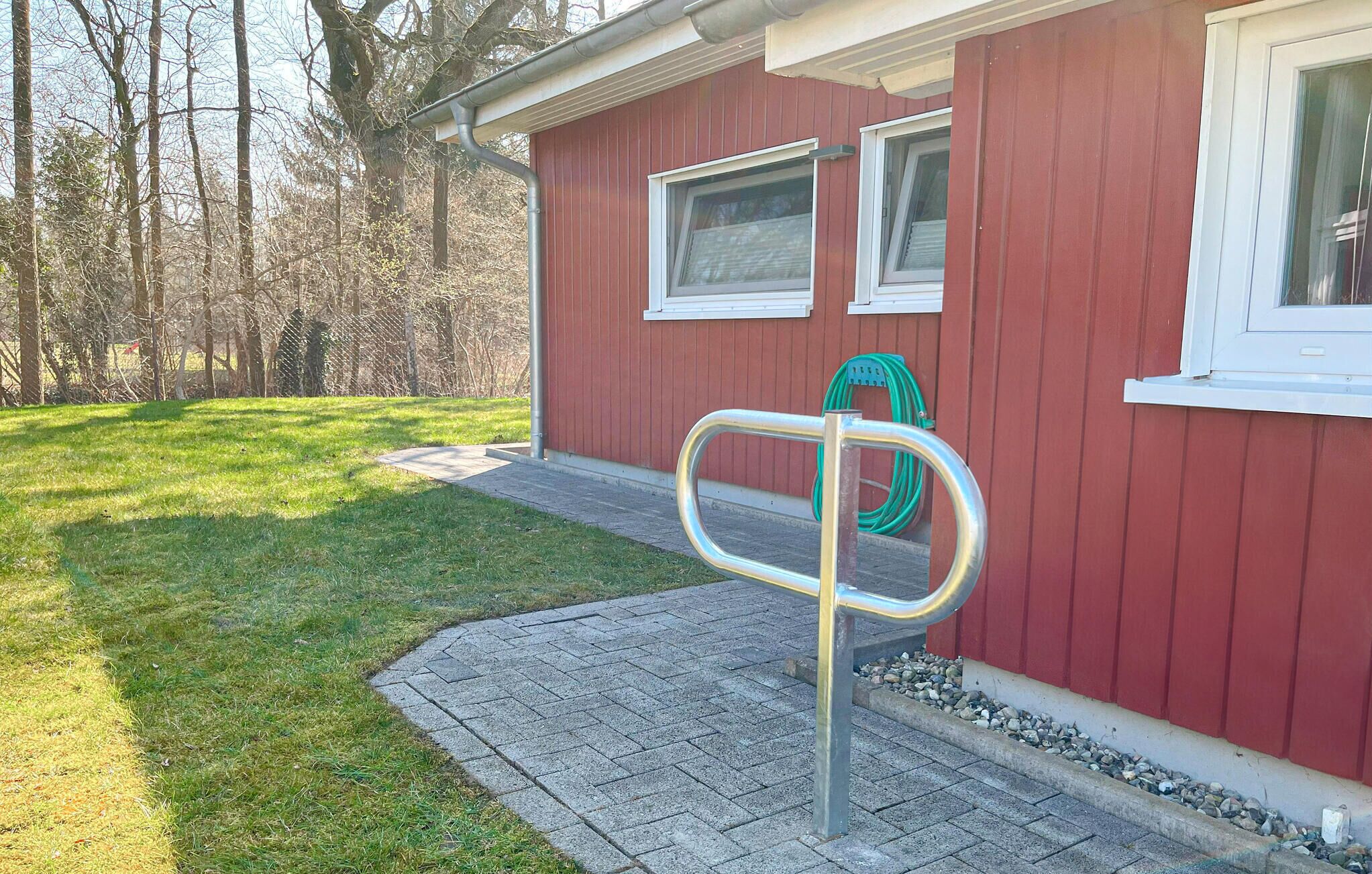 Un bâtiment rouge avec une grille en métal, un tuyau d’arrosage et un chemin pavé.