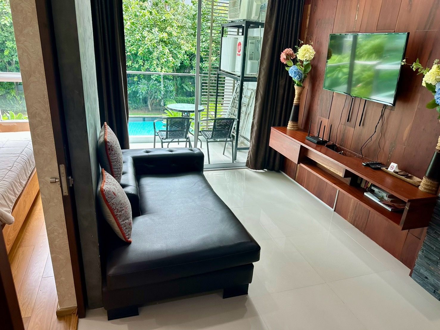 Una sala de estar moderna con un sofá, un televisor instalado en una pared de madera y vistas a una piscina exterior.