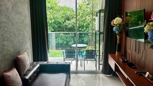 Una sala de estar moderna con un sofá, un televisor de pantalla plana y un balcón con vistas a la vegetación.