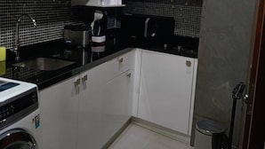 Una cocina moderna con armarios blancos, una encimera negra, una cafetera y una lavadora.