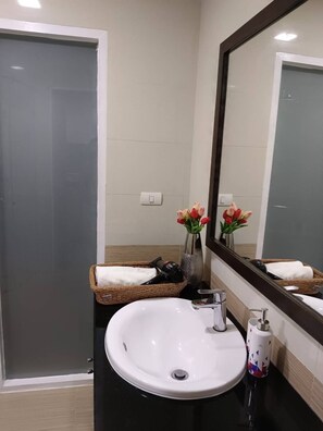 Un baño con un lavabo blanco, un espejo, una ducha y un florero con flores.