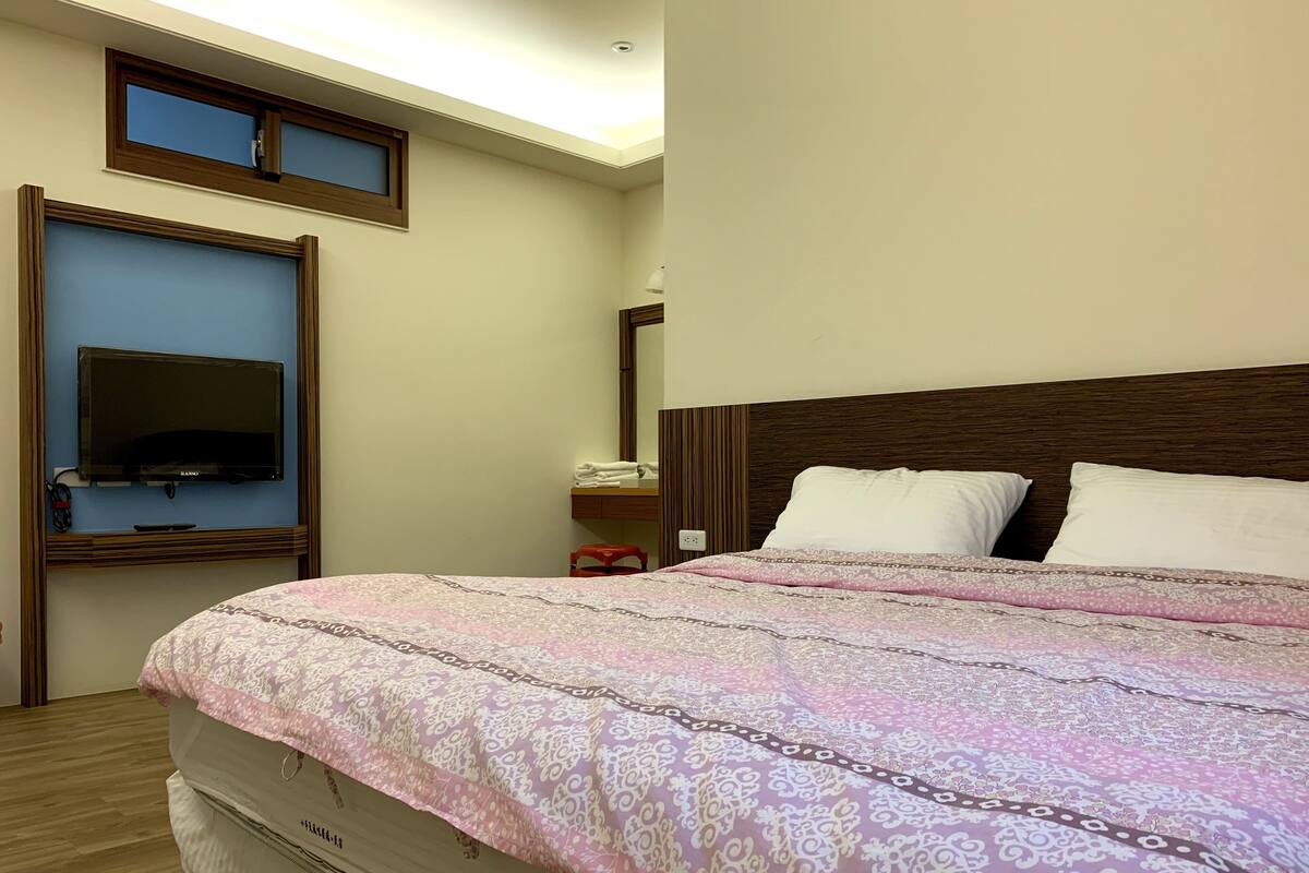 A hotel room with a large bed, a television mounted on the wall, a bedside table, and a window.
