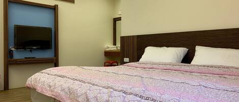 A hotel room with a large bed, a television mounted on the wall, a bedside table, and a window.
