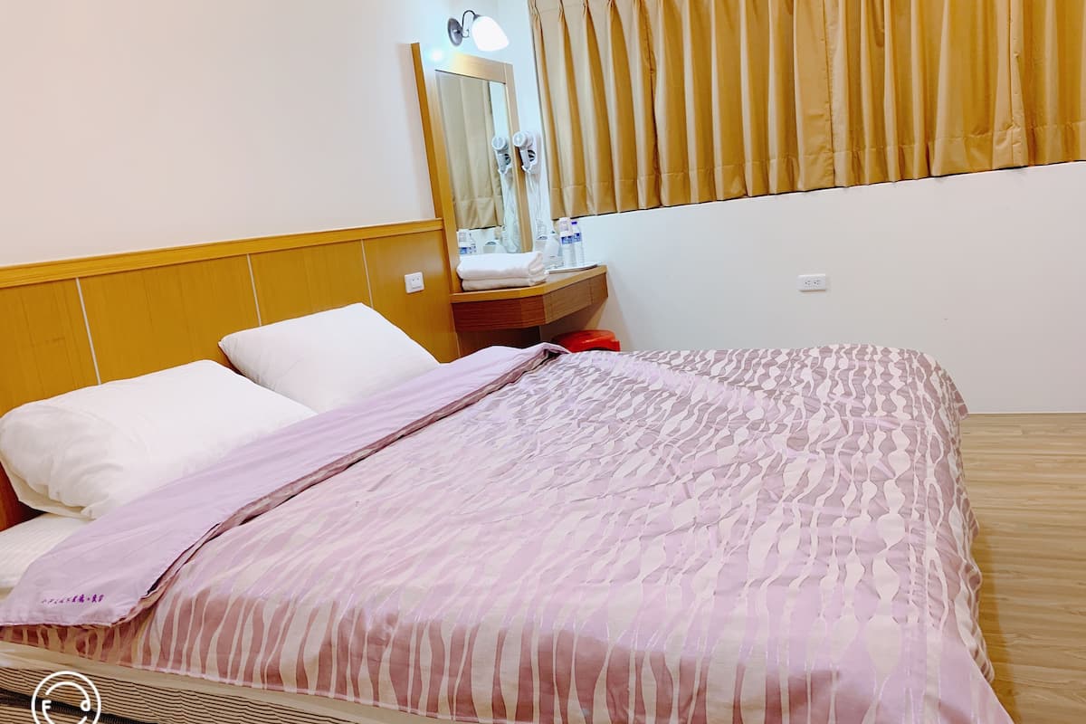 A hotel room with a bed, a nightstand, a mirror, and a window with curtains.