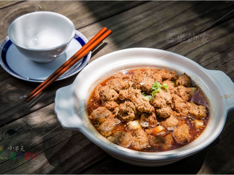 A bowl of soup with meatballs and a cup with chopsticks on a wooden table.
