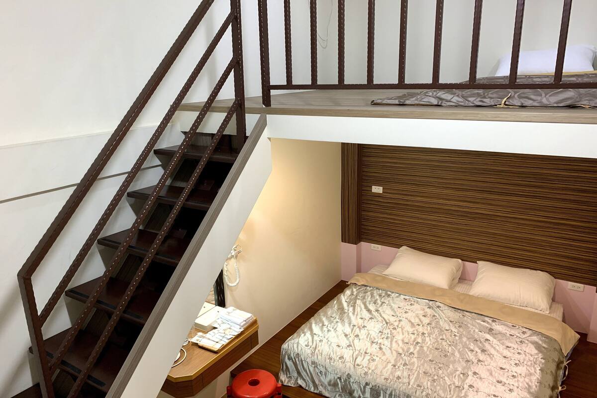 A compact room with a bunk bed, a desk with a chair, and a staircase.