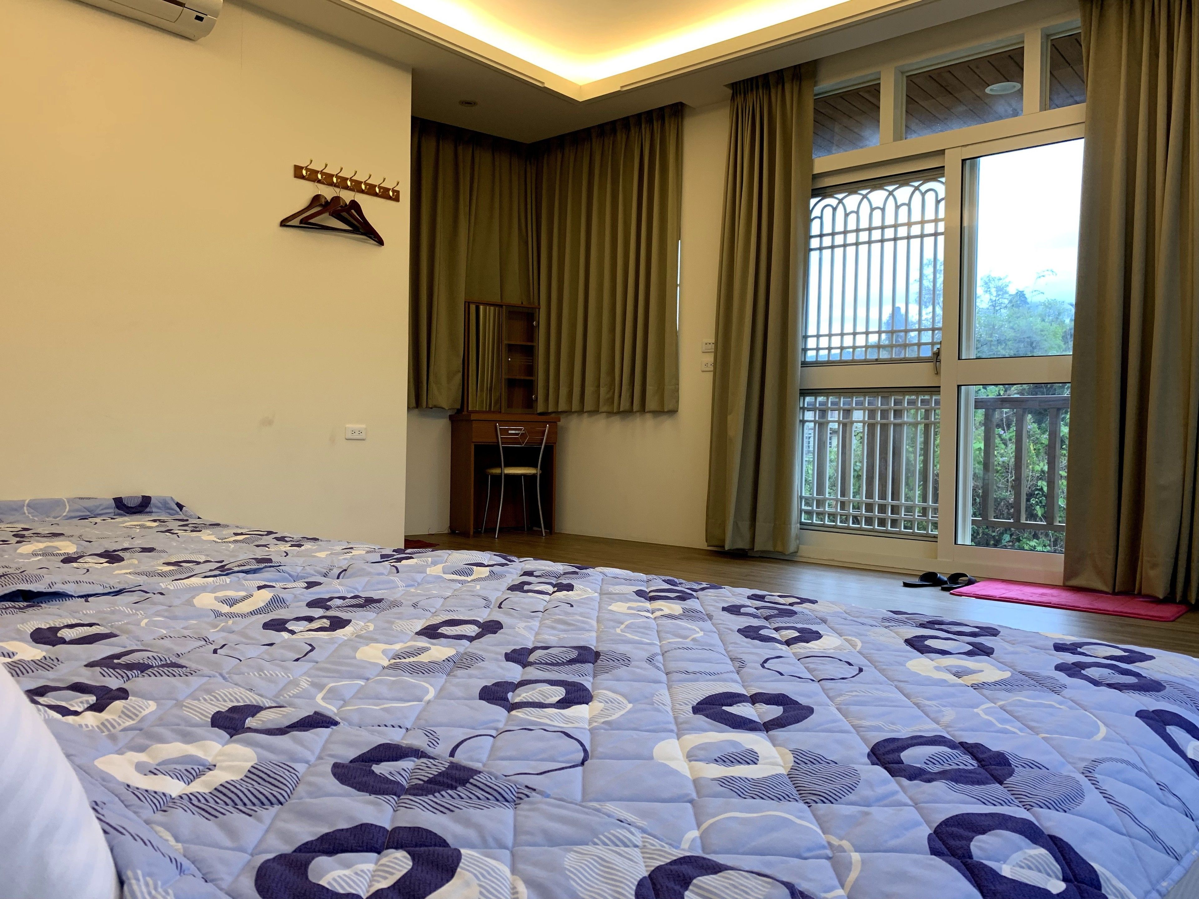 A bedroom with a bed, a desk, and a window with curtains.
