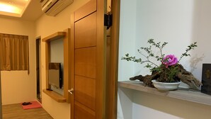A hallway with a wooden door, a potted plant with a pink flower, and a red mat on the floor. - Jia's Homestay (Lugu)