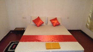 Uma cama com um cobre-leito vermelho e branco, duas almofadas vermelhas e uma pequena mesa de cabeceira de madeira com uma lâmpada.