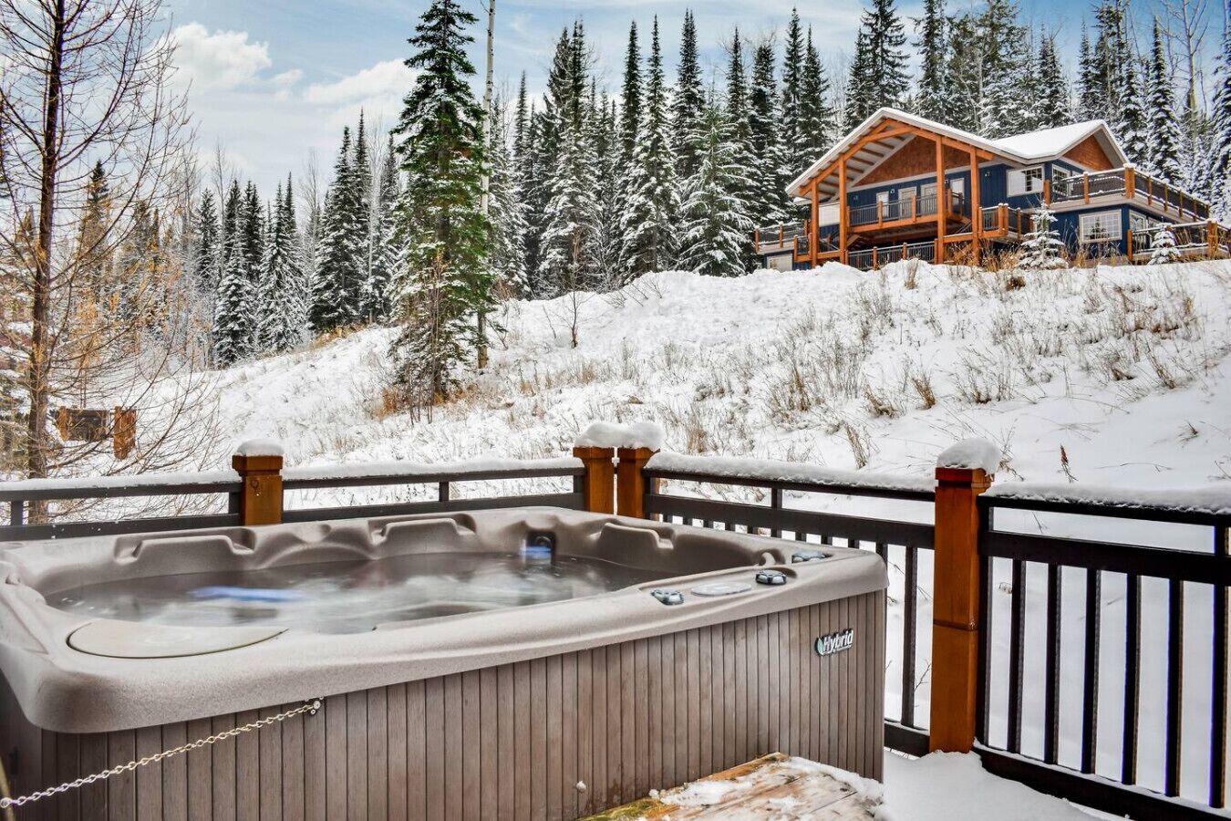 Una vasca idromassaggio su un pontile di legno con vista su un lodge in una foresta innevata.
