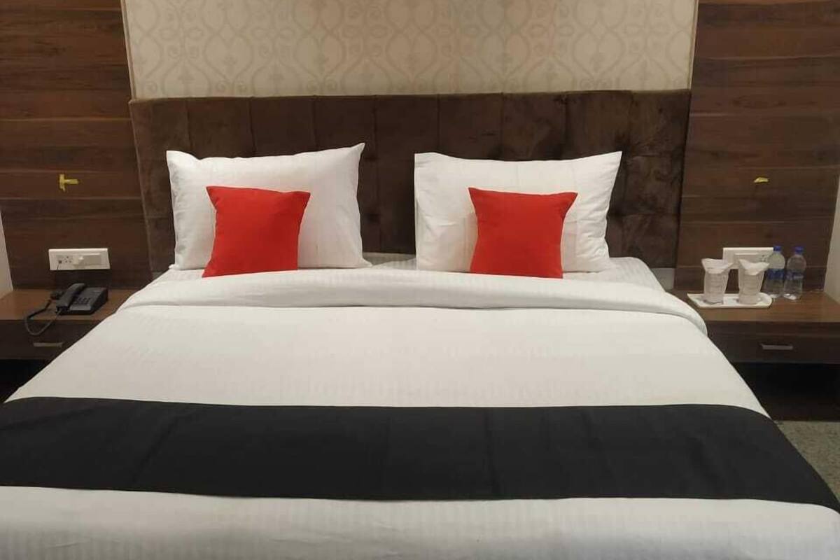 A hotel room with a large bed, a wooden headboard, and a nightstand with a phone and water bottles.