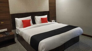 Habitación de hotel con una cama grande, dos almohadas, una mesita de noche con teléfono y una mesita auxiliar.