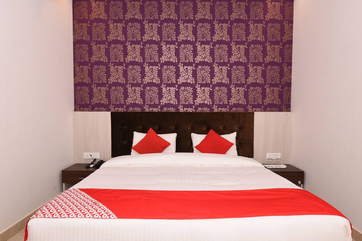 A neatly made bed with a red and white bedspread, two red pillows, and a headboard with a purple floral pattern.