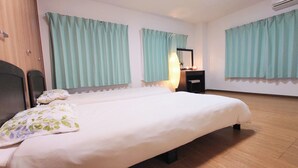 A hotel room with a large bed, a wooden wardrobe, a desk with a mirror, and light green curtains. - 3A Spacious room with Built-in Kitchen (Ōsaka-shi)