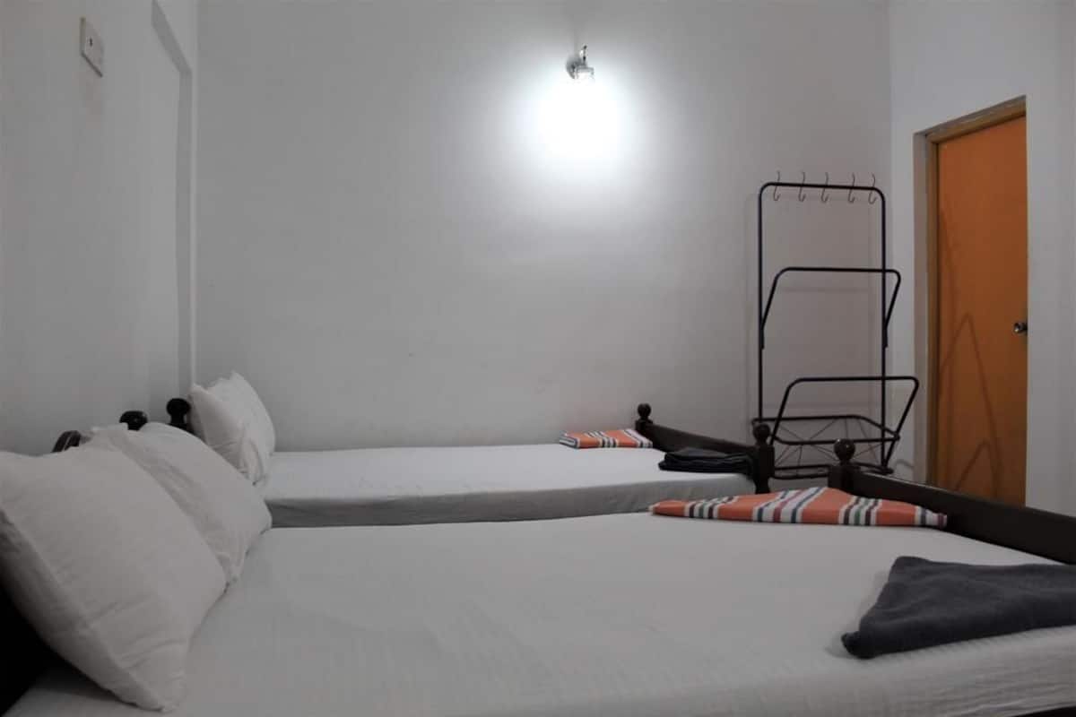 A room with two single beds, a metal drying rack, a wooden door, and a light fixture on the ceiling.