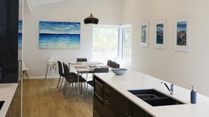 Eine moderne Küche mit einer großen Kochinsel, weißen Schränken und Blick ins Freie durch ein Fenster.