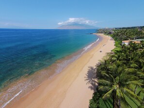 A beach with clear blue water, a sandy shore, and a hotel in the background. - Kihei Getaway in Paradise (Kihei)