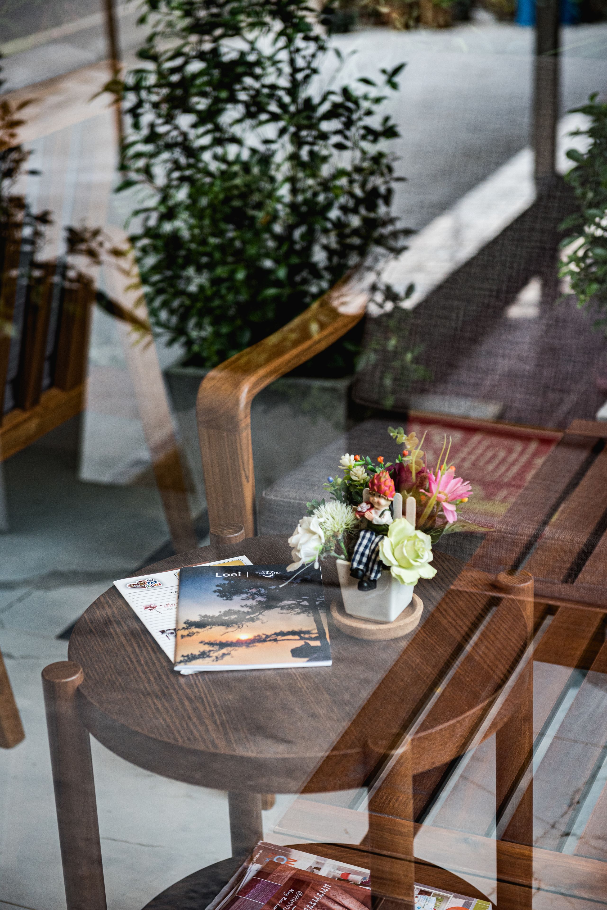 A wooden bench with a small table in front, holding a book, a vase with flowers, and some papers.